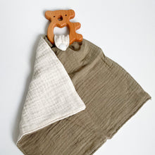 Load image into Gallery viewer, a wooden koala teether attached to a dark olive muslin comforter folded showing white underside