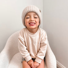 Load image into Gallery viewer, a toddler sitting sticking his tongue out wearing the crew sweatshirt in eggnog and toddler beanie in oatmeal