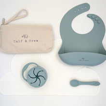 Load image into Gallery viewer, Beige pouch with Calf & Crew logo, snack cup, spoon and silicone bib in baby blue colour on top of a white silicone mat