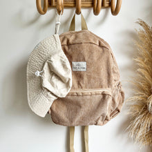 Load image into Gallery viewer, a everyday sunhat in sand hanging on a wooden hook with a sand coloured corduroy backpack