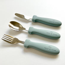 Load image into Gallery viewer, the stainless steel kids cutlery set showing a fork, spoon and knife in baby blue silicone with the calf & crew logo