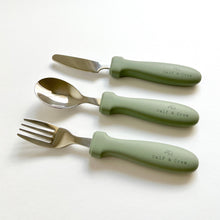 Load image into Gallery viewer, the stainless steel kids cutlery set showing a fork, spoon and knife in sage silicone with the calf & crew logo
