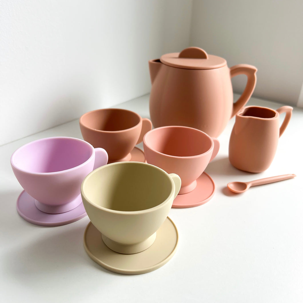 the silicone toy tea set in sunrise colour showing the four different coloured teacups & saucers, a peach coloured milk jug, stiring spoon, and teapot