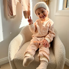Load image into Gallery viewer, a child sitting in a soft white chair smiling wearing the tracksuit romper in peach striped
