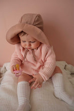 Load image into Gallery viewer, a baby sitting against a pink wall wearing the floppy sun hat in rose colour with the front flipped up
