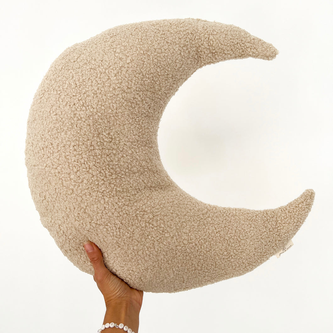 a hand holding up an oat coloured boucle moon feeding pillow
