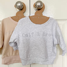 Load image into Gallery viewer, crew sweatshirts hanging on calf & crew hangers in blizzard and eggnog colour