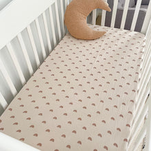 Load image into Gallery viewer, a white cot with a rainbow organic fitted cot sheet and a tan moon pillow