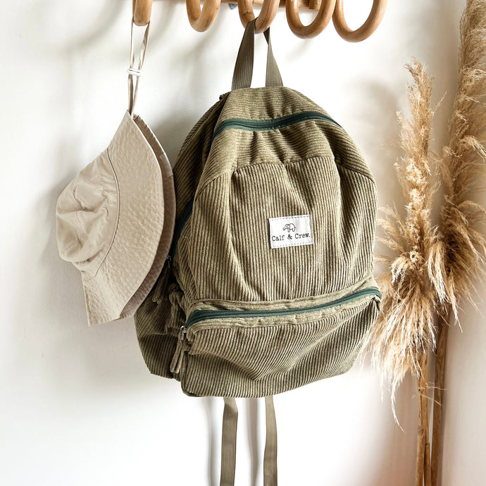 a everyday sunhat in sand hanging on a wooden hook with a khaki coloured corduroy backpack