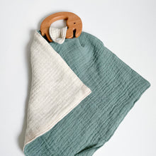 Load image into Gallery viewer, a wooden elephant teether attached to a teal muslin comforter folded showing white underside