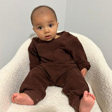 Load image into Gallery viewer, a baby sitting in a soft white chair wearing the tracksuit romper in coffee colour
