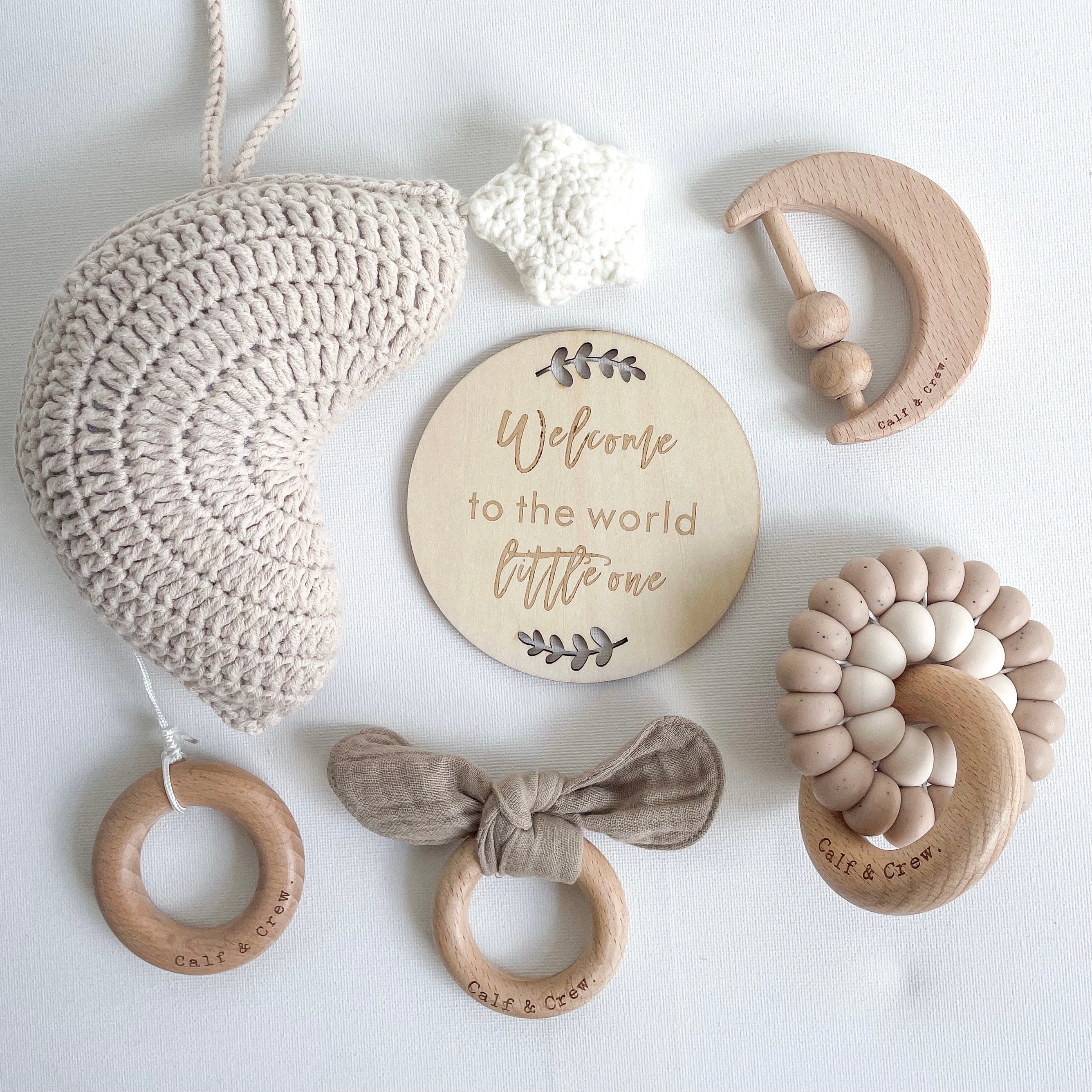 a dusk coloured crochet moon musical pull toy, a muslin bunny ear teether in taupe, a wooden moon rattle, a double silicone ring teether in chai colour around a
