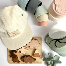 Load image into Gallery viewer, A crew cap in cream colour, silicone stacking cups spilled to the side, a wooden dinosaur puzzle, and a collapsible snack cup and easy grip spoon and fork in sage colour