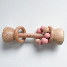 Load image into Gallery viewer, a wooden rattle with a blush  silicone teether ring and the calf &amp; crew logo engraved on the center
