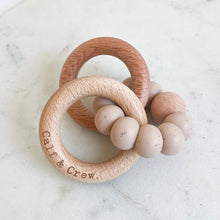 Load image into Gallery viewer, a wooden teether with a chai silicone ring and the calf & crew logo engraved on it