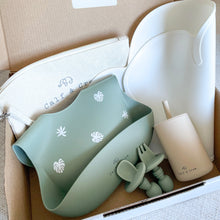 Load image into Gallery viewer, a box filled with beige bag, white silicone mat folded, forest green bib, small spoon and fork, and silicone straw cup in sand colour