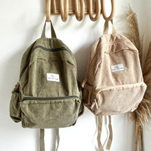 Load image into Gallery viewer, a khaki and sand coloured corduroy backpacks hanging on wooden hooks
