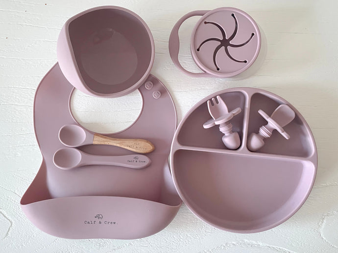 a suction bowl, a bib, a silicone spoon, a beechwood spoon, a collapsible snack cup, a suction divider plate, and easy grip cutlery all in rose silicone colour