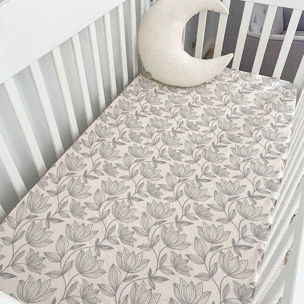 a white cot with a waterlily organic fitted cot sheet and a white moon pillow