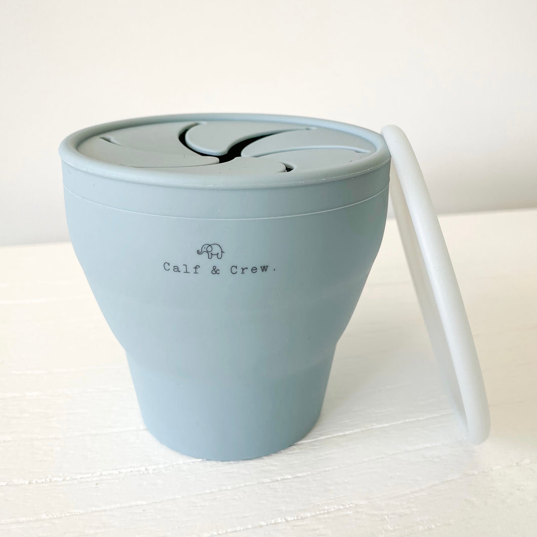 expanded collapsible snack cup with Calf & Crew logo in baby blue, with a white lid leaning against it