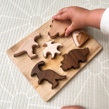 Load image into Gallery viewer, a child&#39;s hand placing a puzzle piece in the base of the wooden dinosaur puzzle
