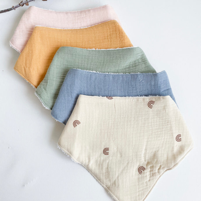 the muslin towel dribble bibs lined up in baby pink, tangerine, sage,, blue and rainbow
