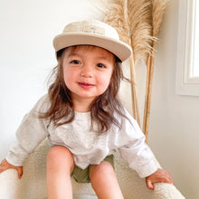 Load image into Gallery viewer, a child sitting in a white soft chair wearing the crew cap patch in cream
