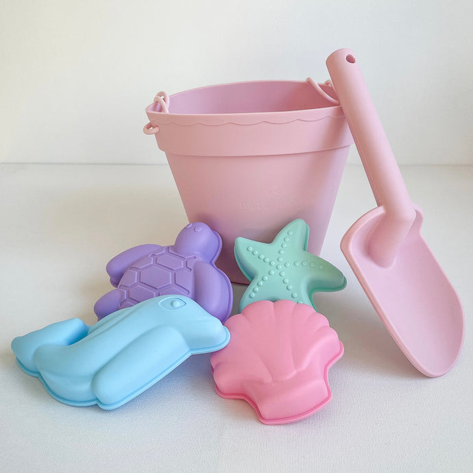 the silicone beach toy set in Flamingo showing the pink bucket and spade, and silicone shape moulds of a turtle, dolphin, starfish and seashell 