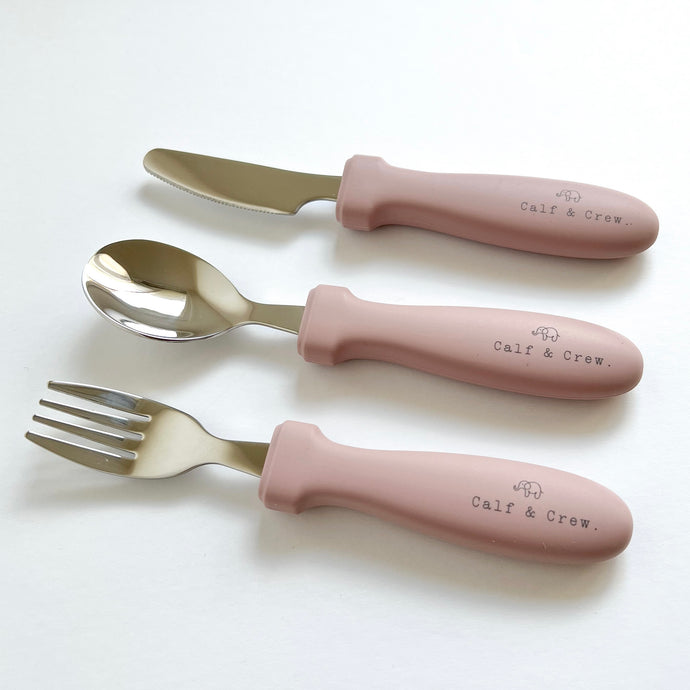 the stainless steel kids cutlery set showing a fork, spoon and knife in rose silicone with the calf & crew logo