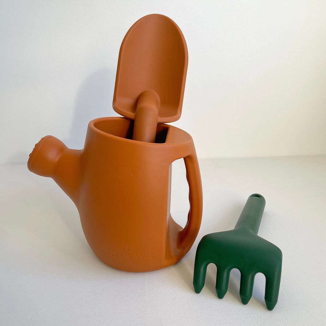 Terracotta silicone garden set showing orange watering can and spade and a green rake
