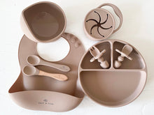 Load image into Gallery viewer, a suction bowl, a bib, a silicone spoon, a beechwood spoon, a collapsible snack cup, a suction divider plate, and easy grip cutlery all in latte silicone colour
