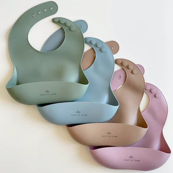 five silicone catcher bibs next to eachother in sage, baby blue, latte and rose