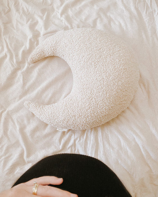 a hand on a pregnant belly leaning over a white boucle moon feeding pillow