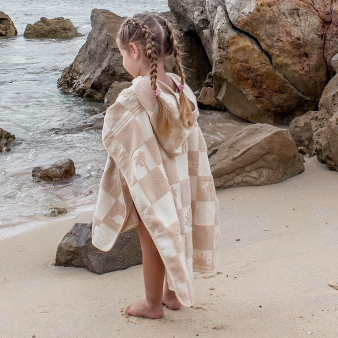 a child wearing the hooded terry beach towel on the sand facing the ocean