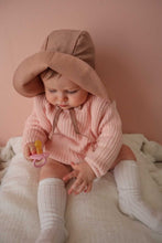 Load image into Gallery viewer, a baby sitting against a pink wall wearing the floppy sun hat in rose colour with the front flipped up

