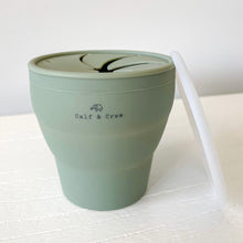 Load image into Gallery viewer, expanded collapsible snack cup with Calf &amp; Crew logo in sage with a white lid leaning against it
