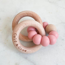 Load image into Gallery viewer, a wooden teether with a blush silicone ring and the calf &amp; crew logo engraved on it
