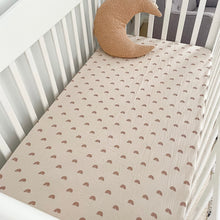 Load image into Gallery viewer, a white cot with a rainbow organic fitted cot sheet and a tan moon pillow
