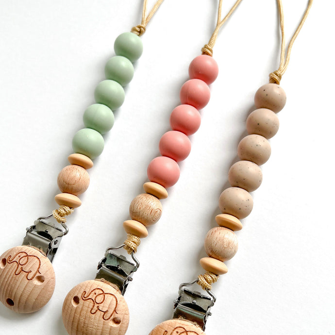 three silicone dummy clips in mint, blush and chai showing the elephant engraved wooden clip