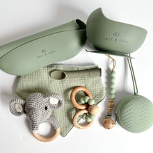 Load image into Gallery viewer, Folded silicone bib and suction bowl, soother case and spoon in sage colour, a wooden silicone ring teether, a silicone dummy clip in mint colour, a grey crochet elephant rattle with a sage muslin bib

