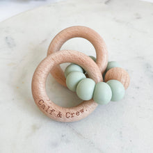 Load image into Gallery viewer, a wooden teether with a mint silicone ring and the calf &amp; crew logo engraved on it
