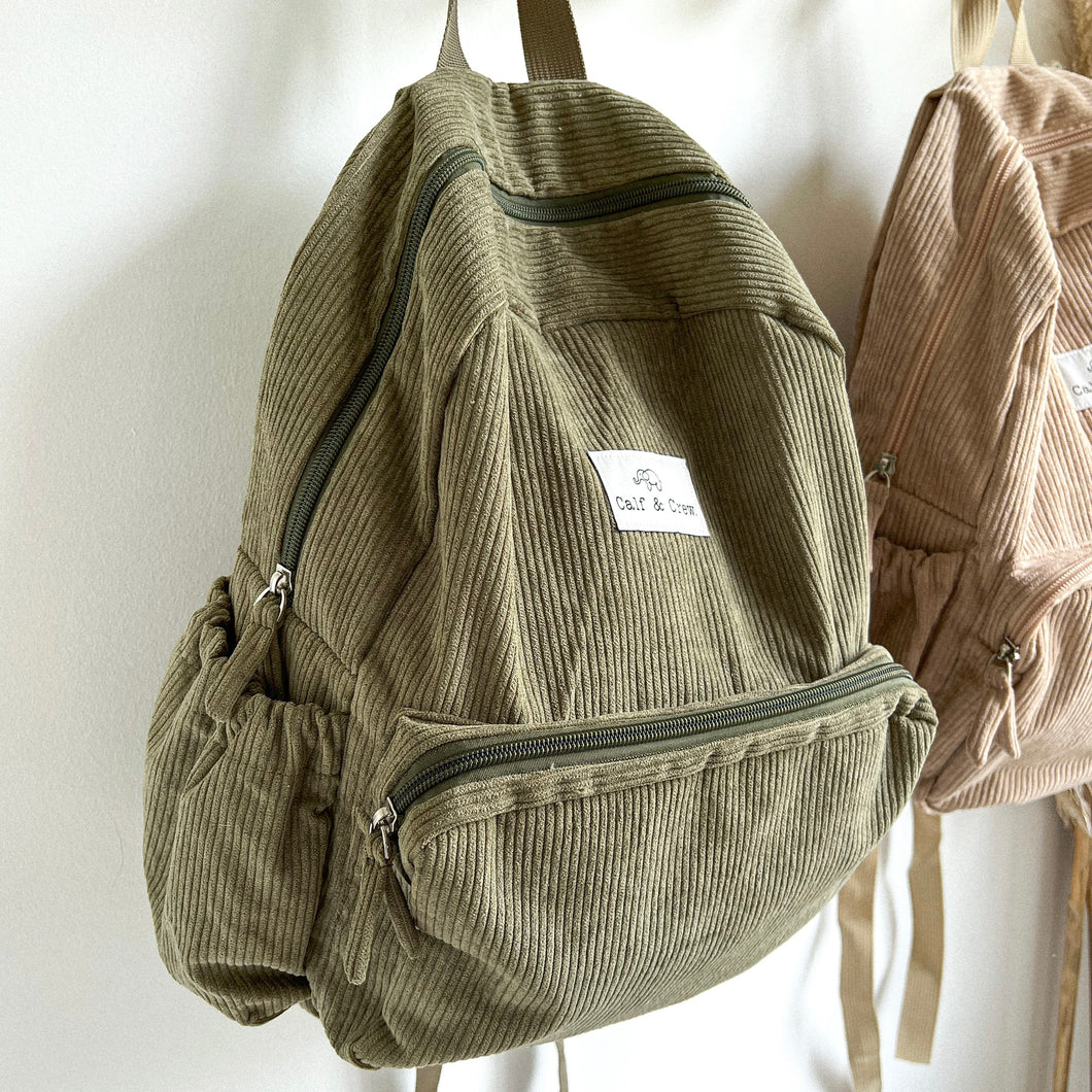 the side view of the khaki corduroy backpack showing the waterbottle pocket and zipper front pocket