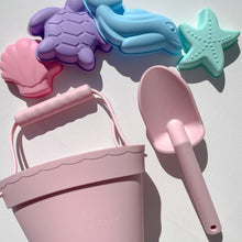 Load image into Gallery viewer, the silicone beach toy set laying flat showing the pink bucket and spade, and shape moulds of a pink seashell, purple turtle, blue dolphin, and teal starfish
