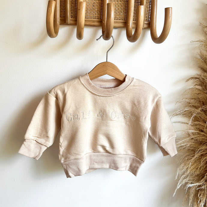 crew sweatshirt in eggnog hanging on a hanger on a wooden hook