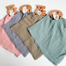 Load image into Gallery viewer, a wooden koala on a coral pink muslin comforter, a wooden elephant on a steel blue muslin comforter, a wooden koala teether on a olive muslin comforter, and a wooden elephant teether on a teal muslin comforter
