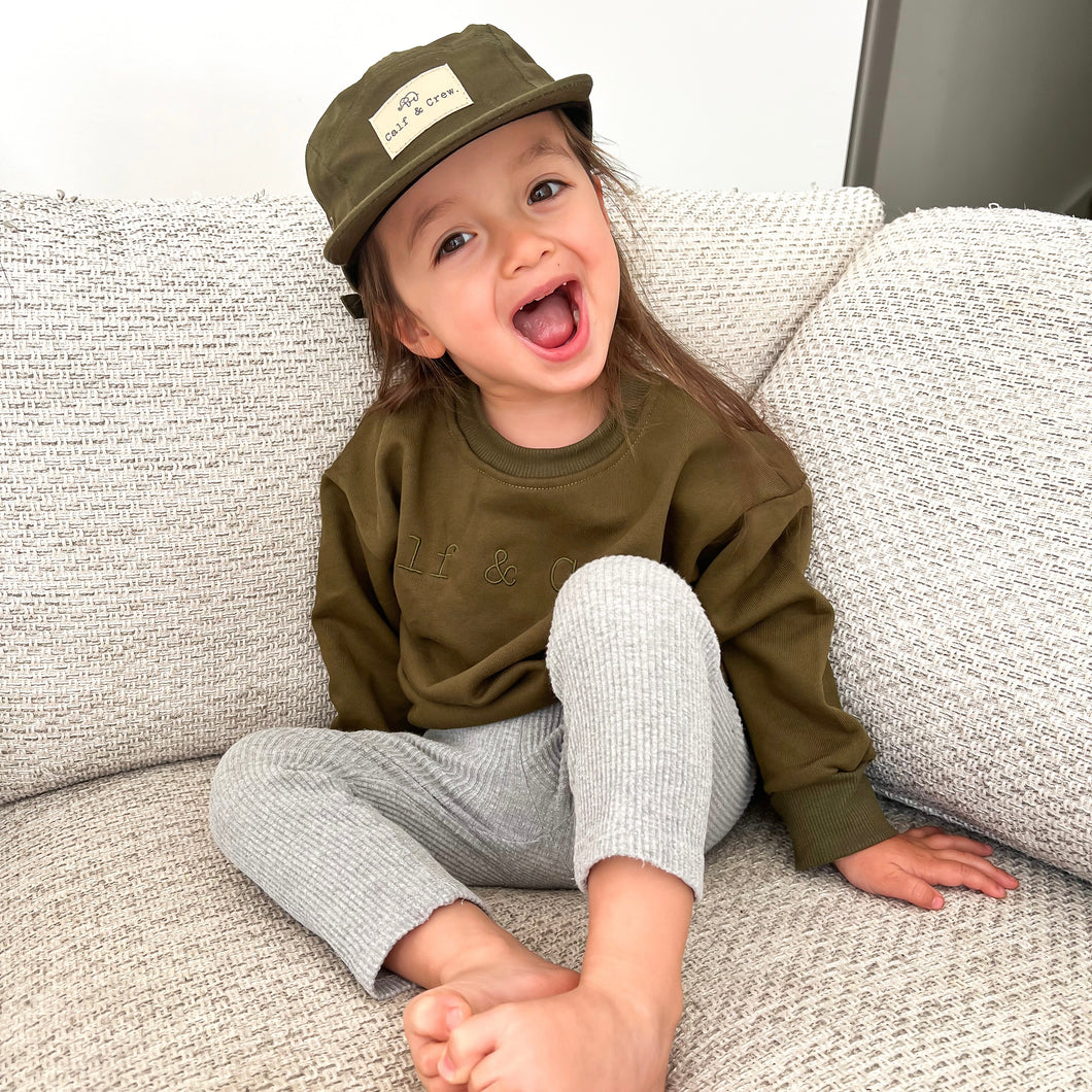 child sitting on a grey lounge wearing the crew sweatshirt in khaki and crew cap patch in khaki