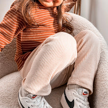 Load image into Gallery viewer, a child sitting in a soft chair showing the ribbed straight fit leggings in beige
