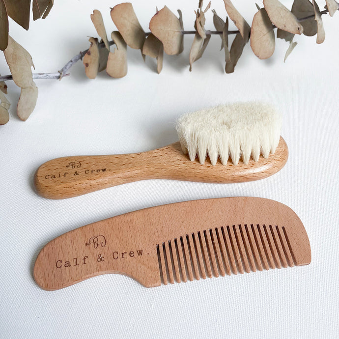a wooden baby brush with white bristles laying next to a wooden baby comb, both with the Calf & Crew logo engraved