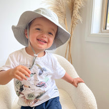 Load image into Gallery viewer, child smiling and wearing the sun hat sitting in a soft white chair
