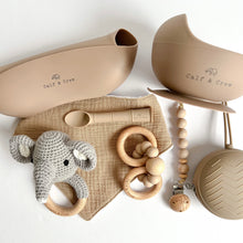 Load image into Gallery viewer, Folded silicone bib and suction bowl, soother case and spoon in latte colour, a wooden silicone ring teether, a silicone dummy clip in chai colour, a grey crochet elephant rattle with a chai muslin bib
